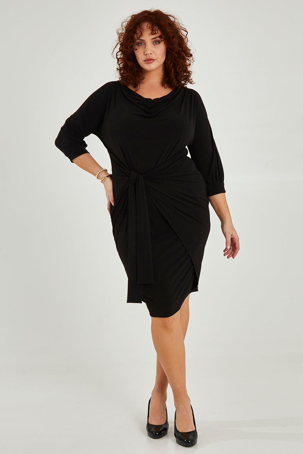 Model Maddy wearing size 16 of the Cowl Tie Drape Dress in colour Black (Black), from the front, showing the whole outfit