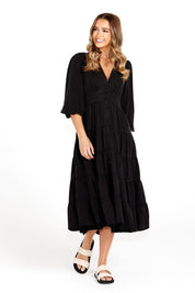 A model wearing the Charity Tiered Midi Dress in colour Black (Black), from the front, showing the whole outfit