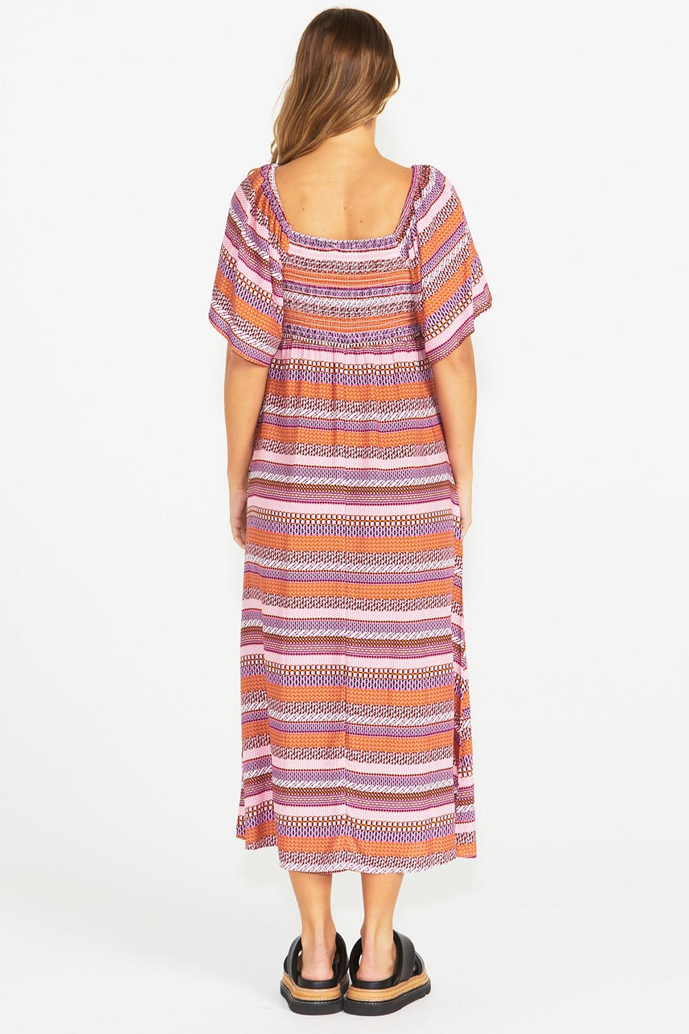 A model wearing the Raquel Midi Dress in colour Aztec (Pink), from the back