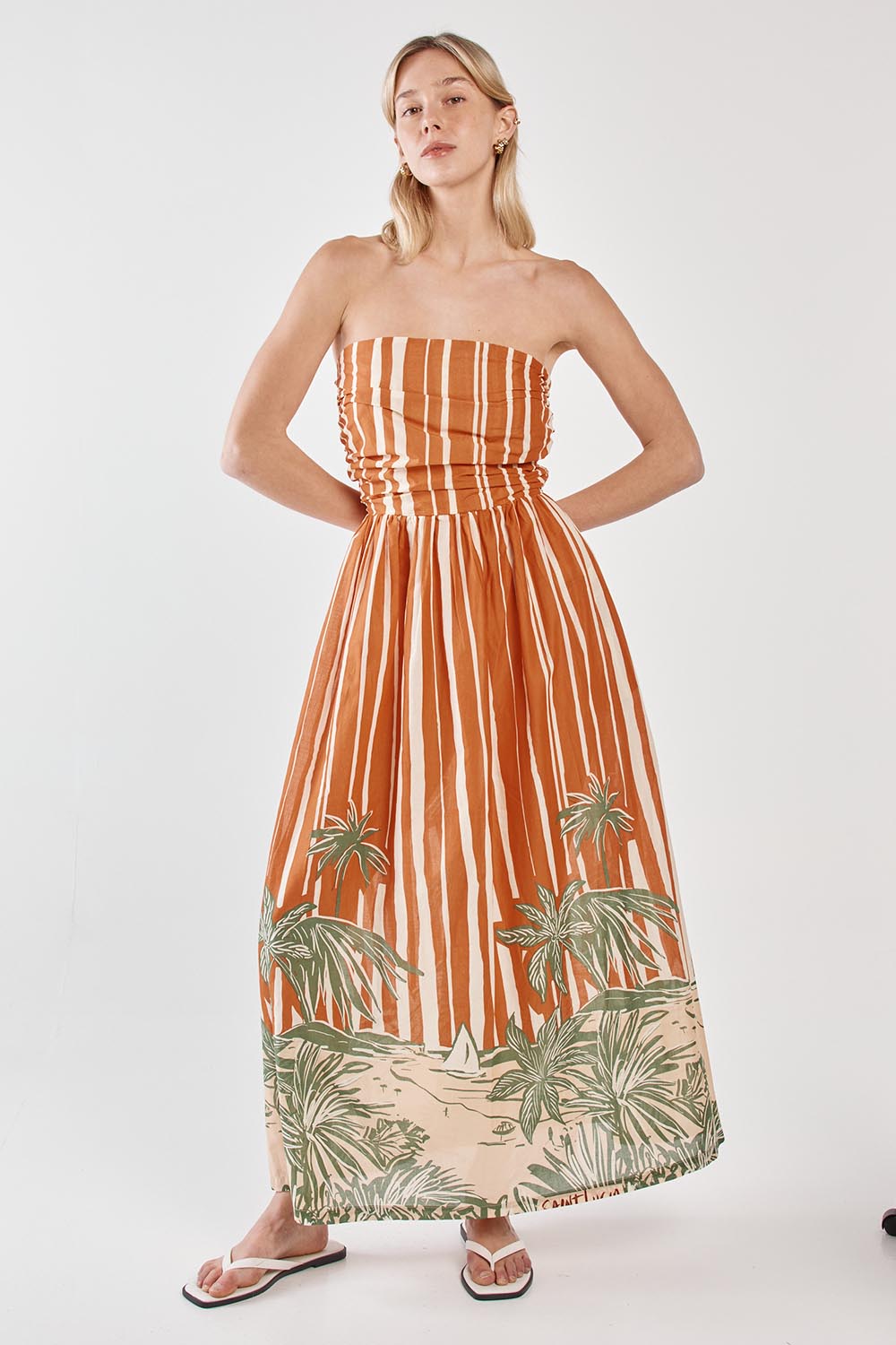 A model wearing the Mina Cotton Strapless Dress in colour Palmstripe, from the front, showing the whole outfit