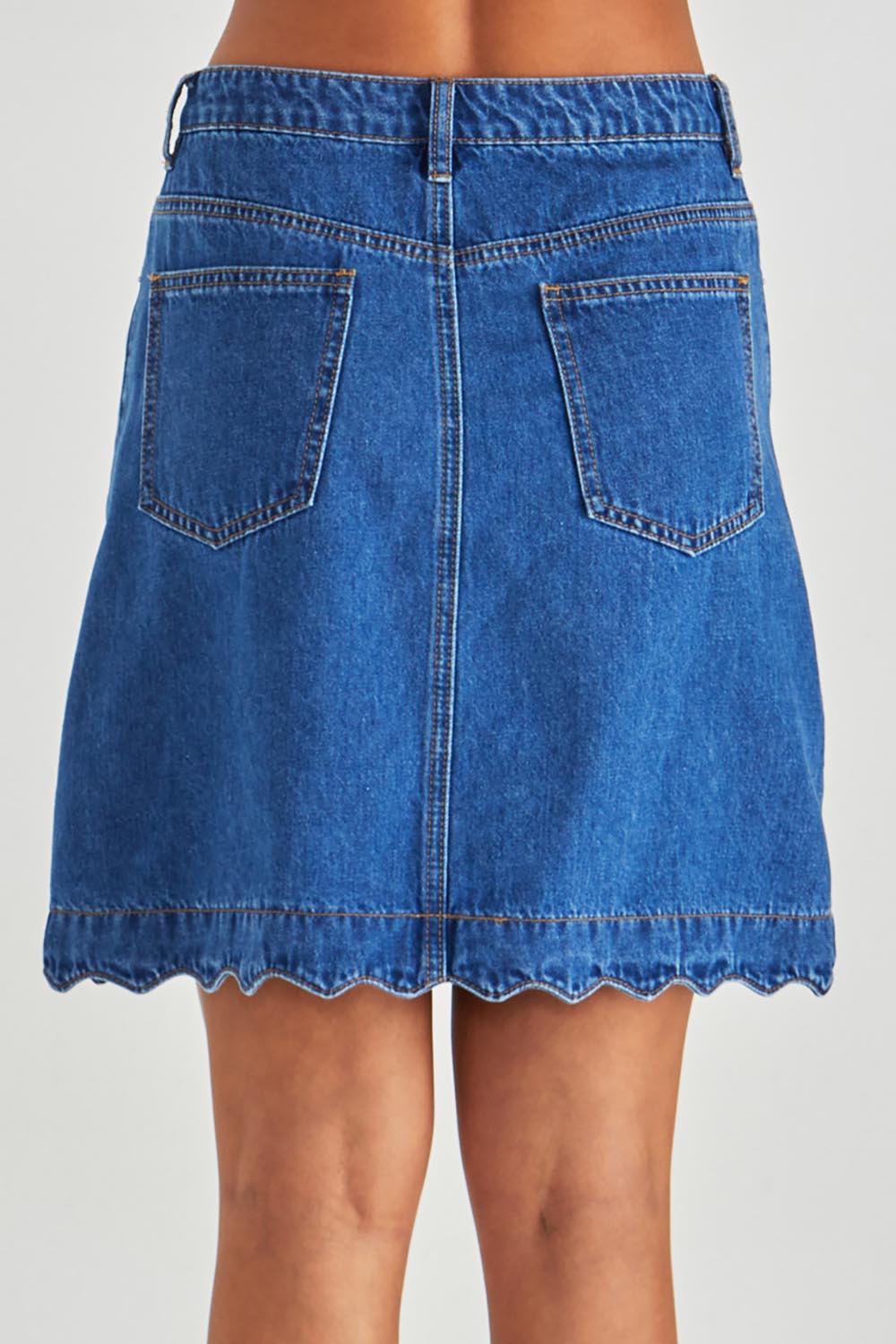 A model wearing the Vale Scalloped Denim Skirt in colour Midblue (Blue), from the back