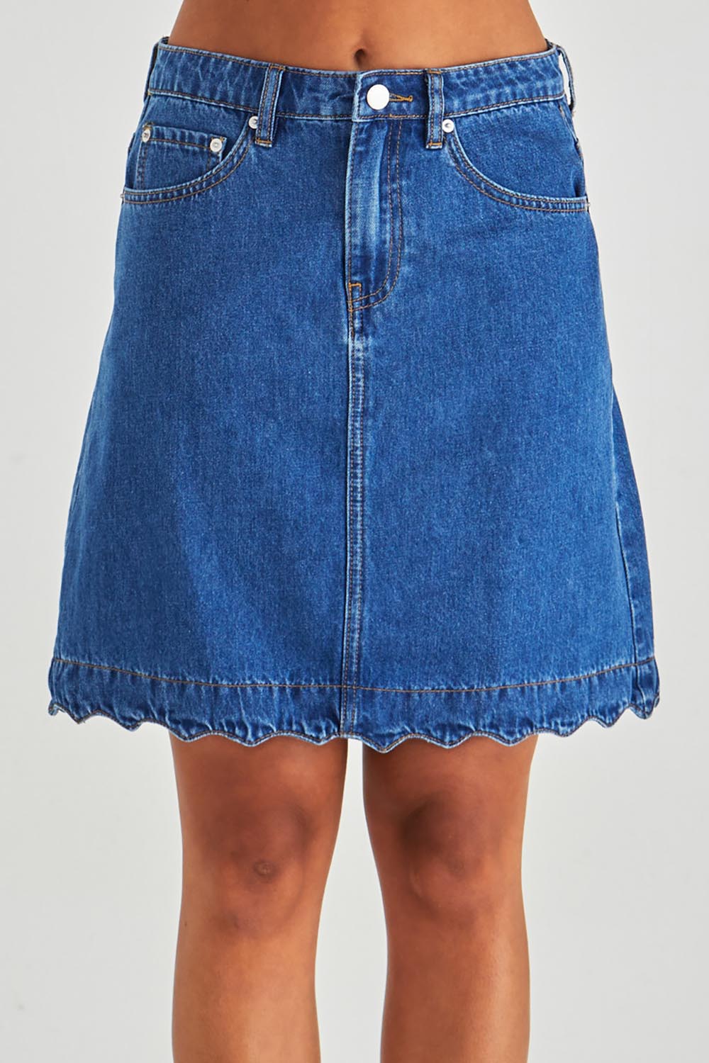 A model wearing the Vale Scalloped Denim Skirt in colour Midblue (Blue), from the front, cropped image