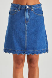 A model wearing the Vale Scalloped Denim Skirt in colour Midblue (Blue), from the front, cropped image