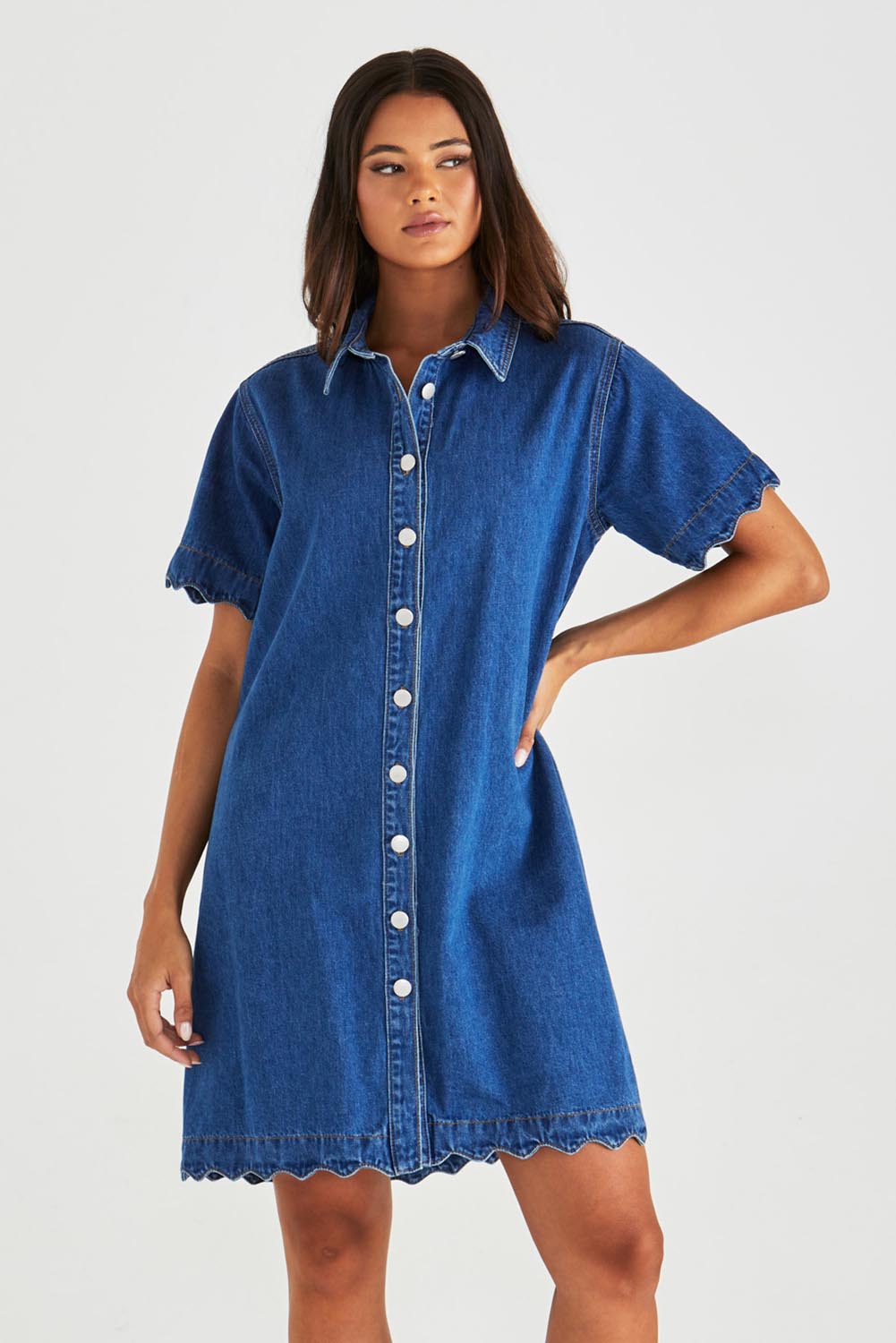 A model wearing the Vale Scalloped Denim Dress in colour Midblue (Blue), from the front, cropped image