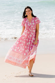 Model Stacey wearing size 10 of the Kurrawa Beach Long Cotton Dress in colour Pinkorange (Pink), from the front, showing the whole outfit