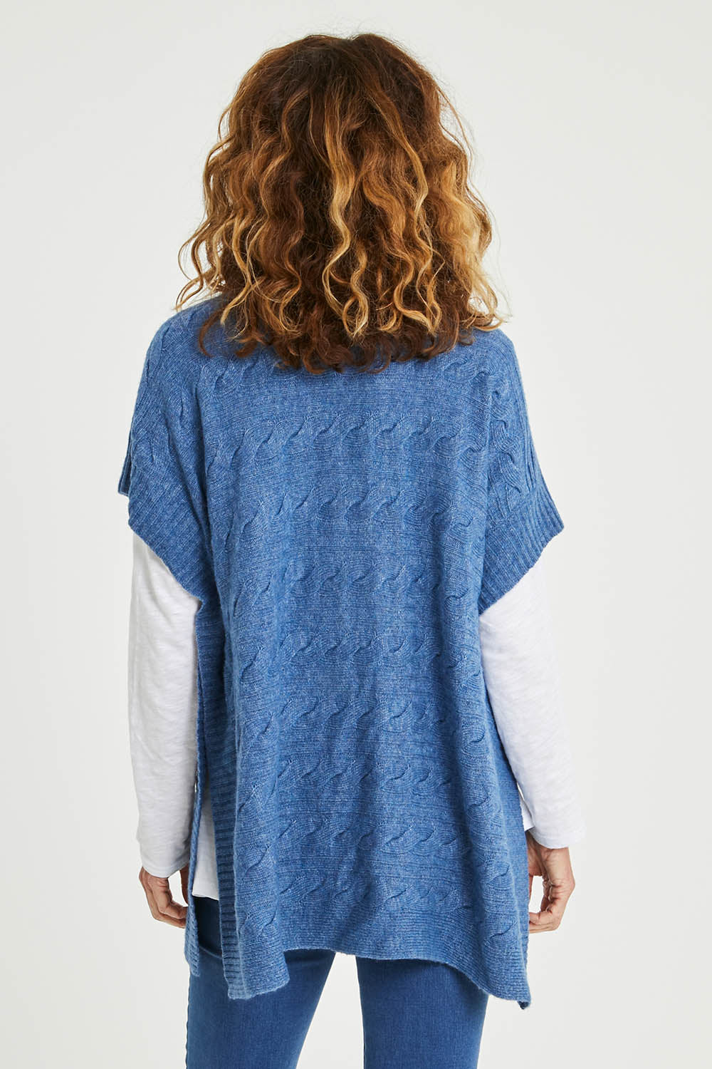 Model Emma wearing size S of the Lambswool Blend Cable Poncho in colour Denim (Blue), from the back