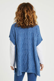 Model Emma wearing size S of the Lambswool Blend Cable Poncho in colour Denim (Blue), from the back