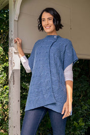 A model wearing the Lambswool Blend Cable Poncho in colour Denim (Blue), from the front, showing the whole outfit