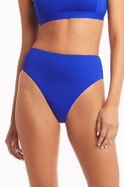 A model wearing the Retro High Waist Pant in colour Cobalt (Blue), from the front, cropped image