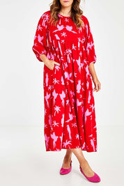 Model Laura wearing size 14 of the Alice Gathered Dress in colour Bird (Red), from the front, cropped image