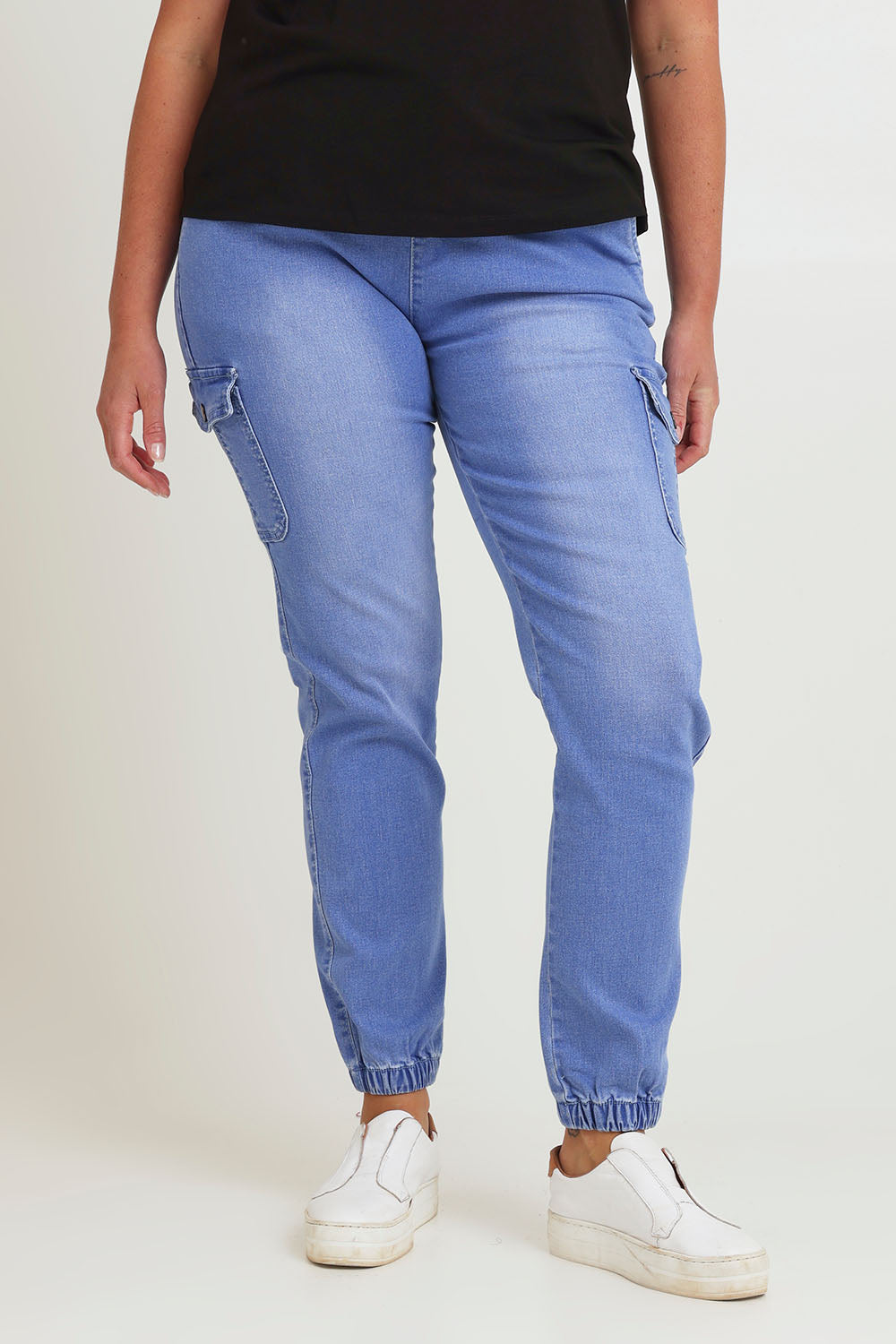 Model Chanel wearing size 16 of the Harlow Cargo Jogger in colour Middenim (Blue), from the front, cropped image